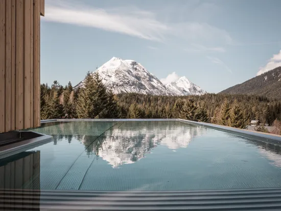Infinity pool reflecting snow-capped mountain and forest at luxury alpine resort